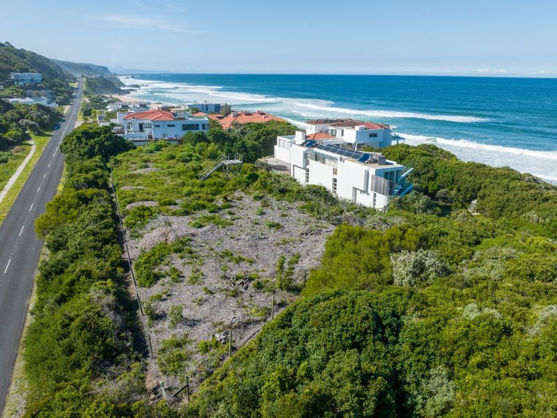 Aerial view of a vacant residential plot situated along the coastline, featuring natural vegetation and proximity to the main road and ocean.