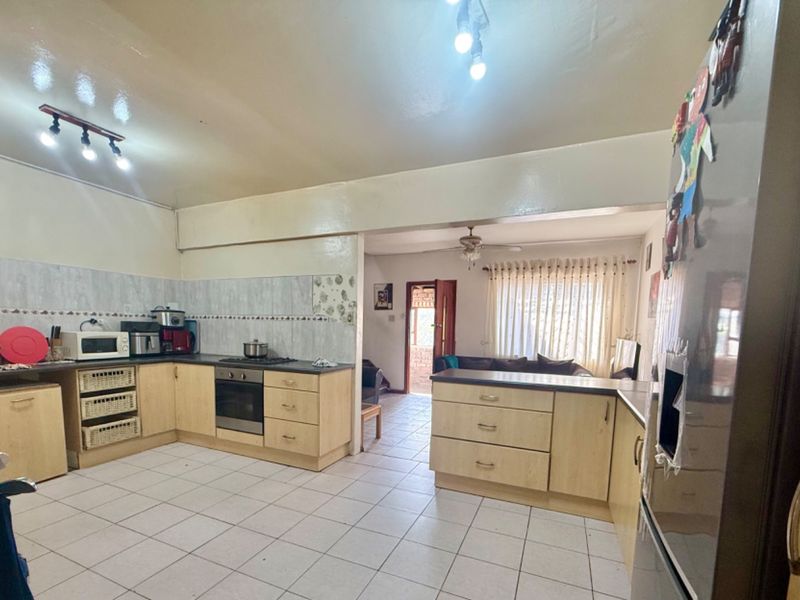 Open-plan kitchen and living area featuring light wood cabinetry, tiled flooring, built-in oven, and a breakfast counter, offering a functional layout.