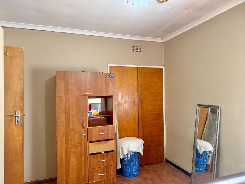 A bedroom featuring tiled flooring, built-in wooden cupboards, and a visible wall crack above the door frame.