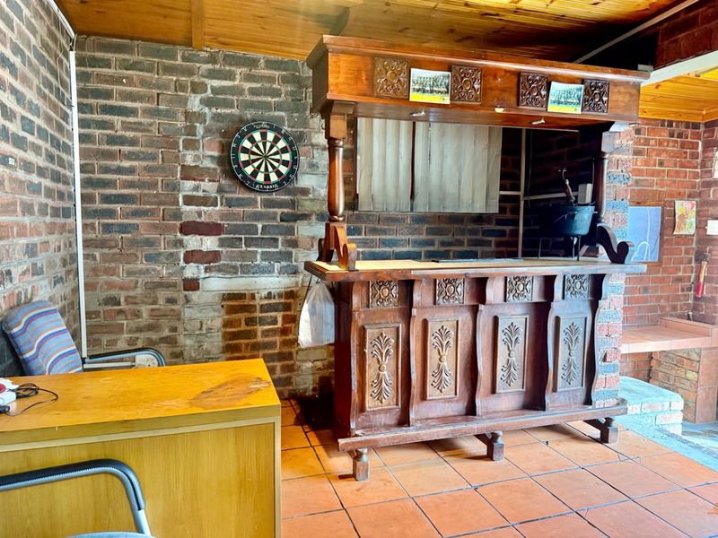 A rustic bar area featuring exposed brick walls, a timber ceiling, and a traditional built-in wooden bar counter with terracotta floor tiles.