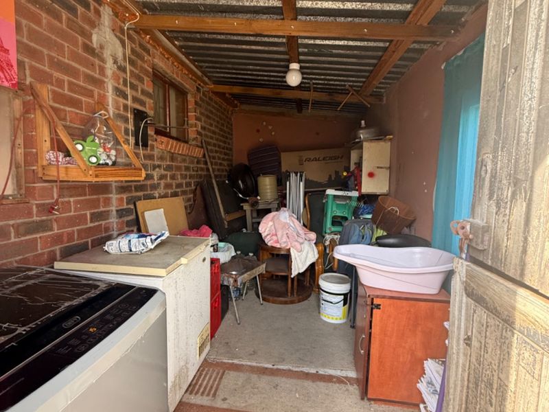 A utility storage space featuring exposed brick walls, a corrugated metal roof, and concrete flooring, currently used for general storage.