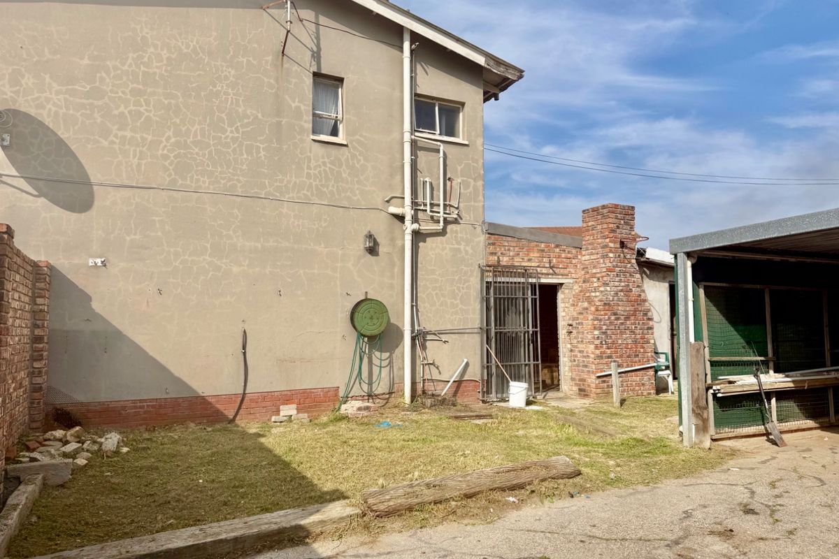 Rear exterior view of the property showing a brick chimney, external plumbing, and a carport structure with visible wall cracking and weathered finishes.