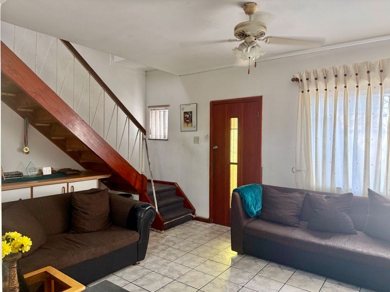 A living room featuring tiled flooring, a timber staircase, and a ceiling fan, offering a functional space with potential for cosmetic updates.