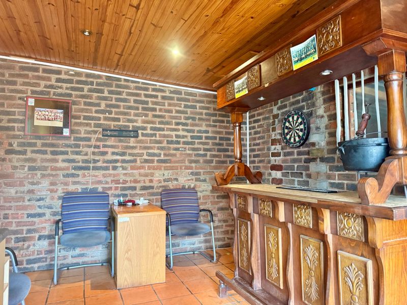A rustic home bar area featuring a built-in wooden counter, exposed brick walls, and a timber-clad ceiling with terracotta floor tiles.
