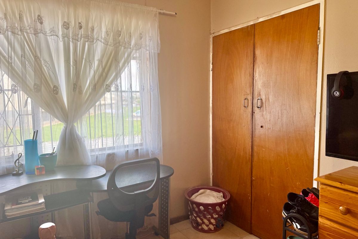 A bedroom featuring tiled flooring, a built-in wooden wardrobe, and a window fitted with security bars.