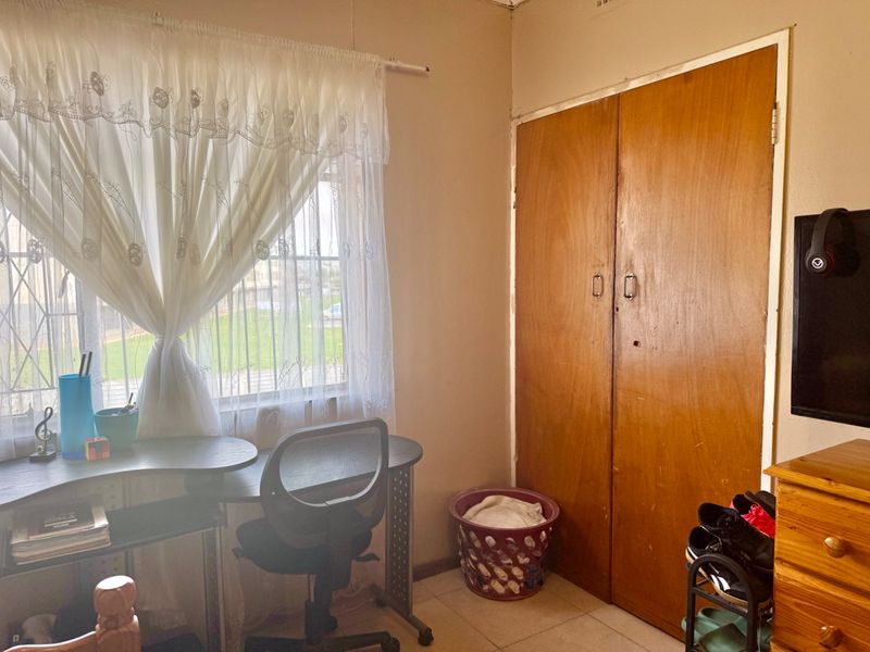 A bedroom featuring tiled flooring, a built-in wooden wardrobe, and a window fitted with security bars.