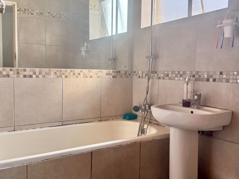 A functional bathroom featuring a pedestal basin, built-in bathtub with shower attachment, tiled finishes, and a large wall mirror.
