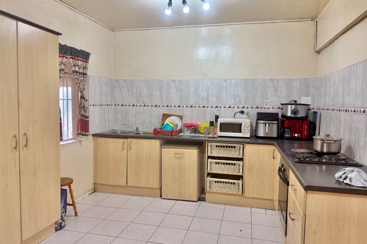 Functional kitchen featuring light wood-look cabinetry, dark laminate countertops, tiled backsplash, and built-in cooking appliances with tiled flooring throughout.