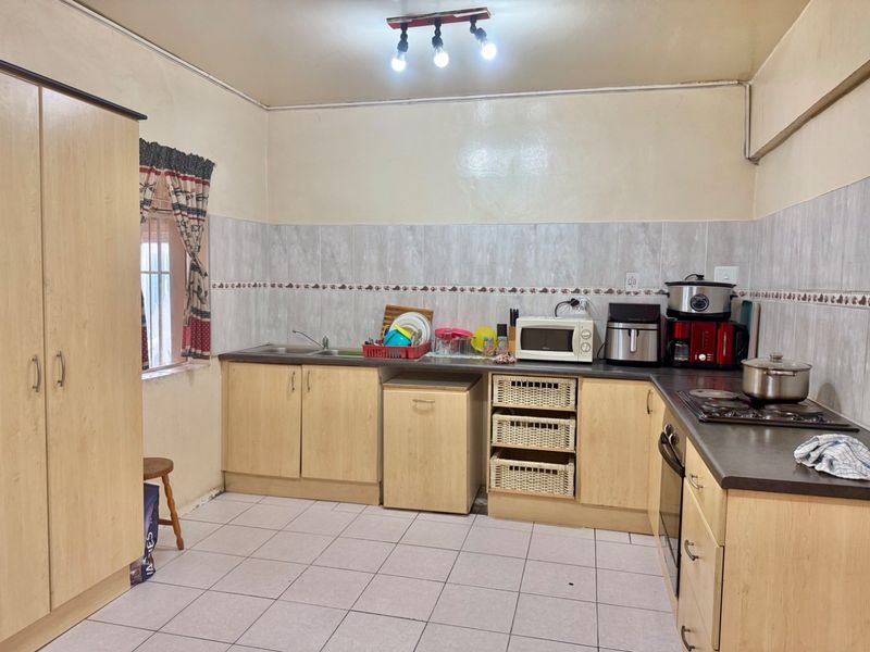 Functional kitchen featuring light wood-look cabinetry, dark laminate countertops, tiled backsplash, and built-in cooking appliances with tiled flooring throughout.