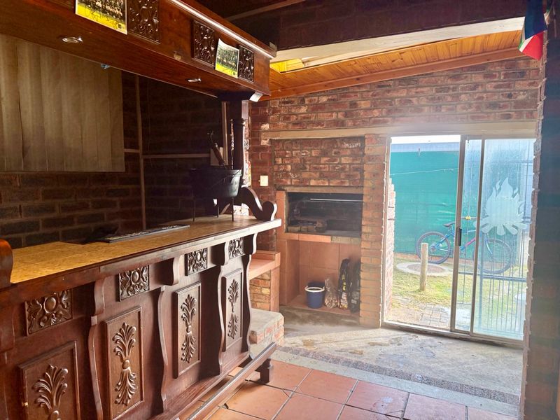 An indoor entertainment area featuring a built-in wooden bar, a traditional brick braai, and direct access to the garden through a sliding glass door.