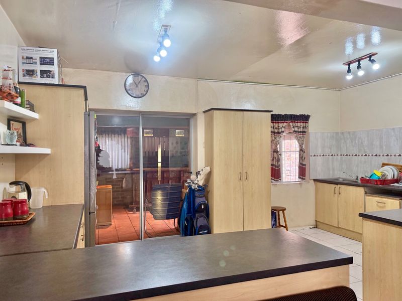 A functional kitchen featuring light wood-finish cabinetry, dark countertops, tiled backsplash, and direct access to an outdoor patio area through sliding glass doors.
