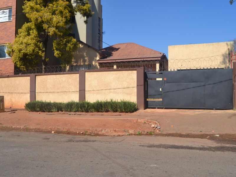 Street view of the property featuring a secure perimeter wall with razor wire and a large metal entrance gate.