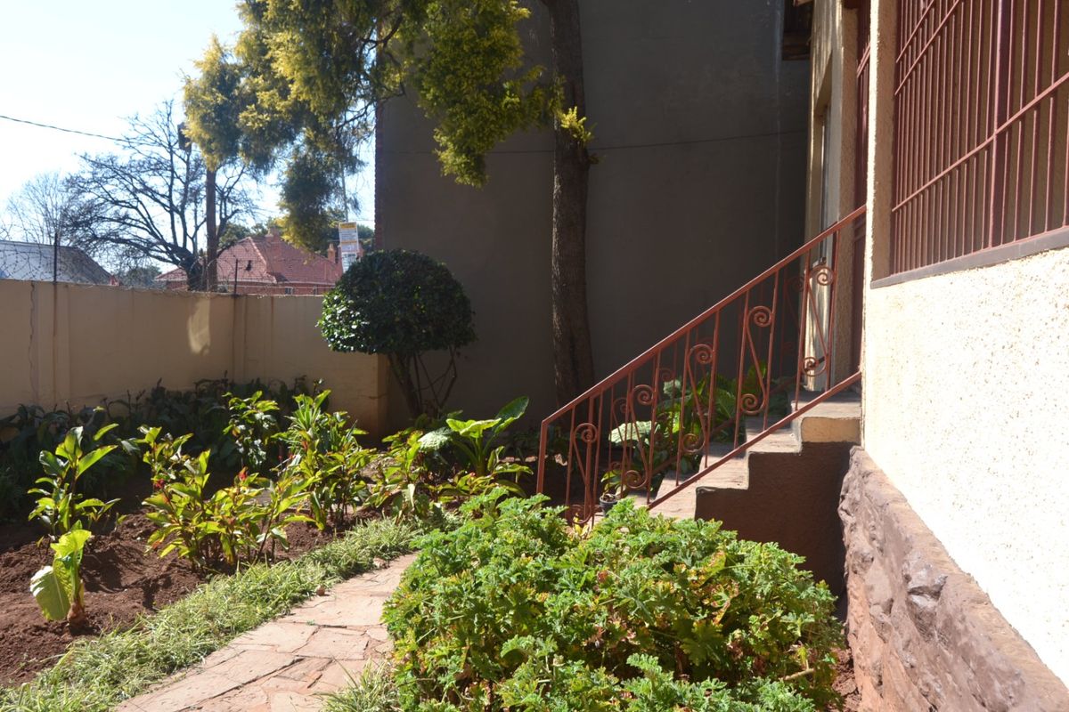 A rear garden area featuring a paved walkway, stone-clad foundation, and a wrought iron staircase leading to the property entrance.