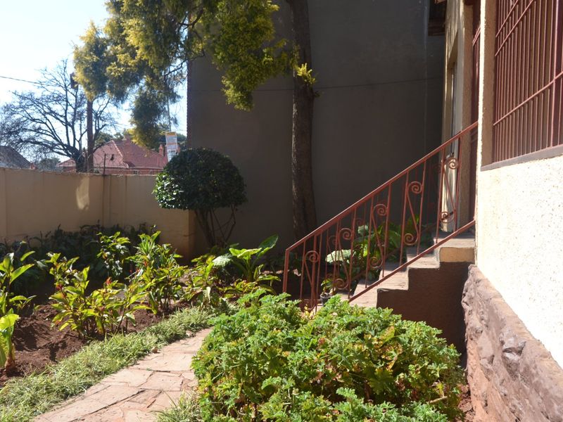 A rear garden area featuring a paved walkway, stone-clad foundation, and a wrought iron staircase leading to the property entrance.