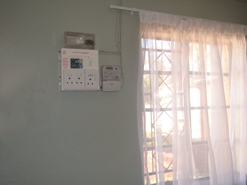 Interior wall featuring a mounted electrical distribution board and prepaid electricity meter, adjacent to a window with security burglar bars.