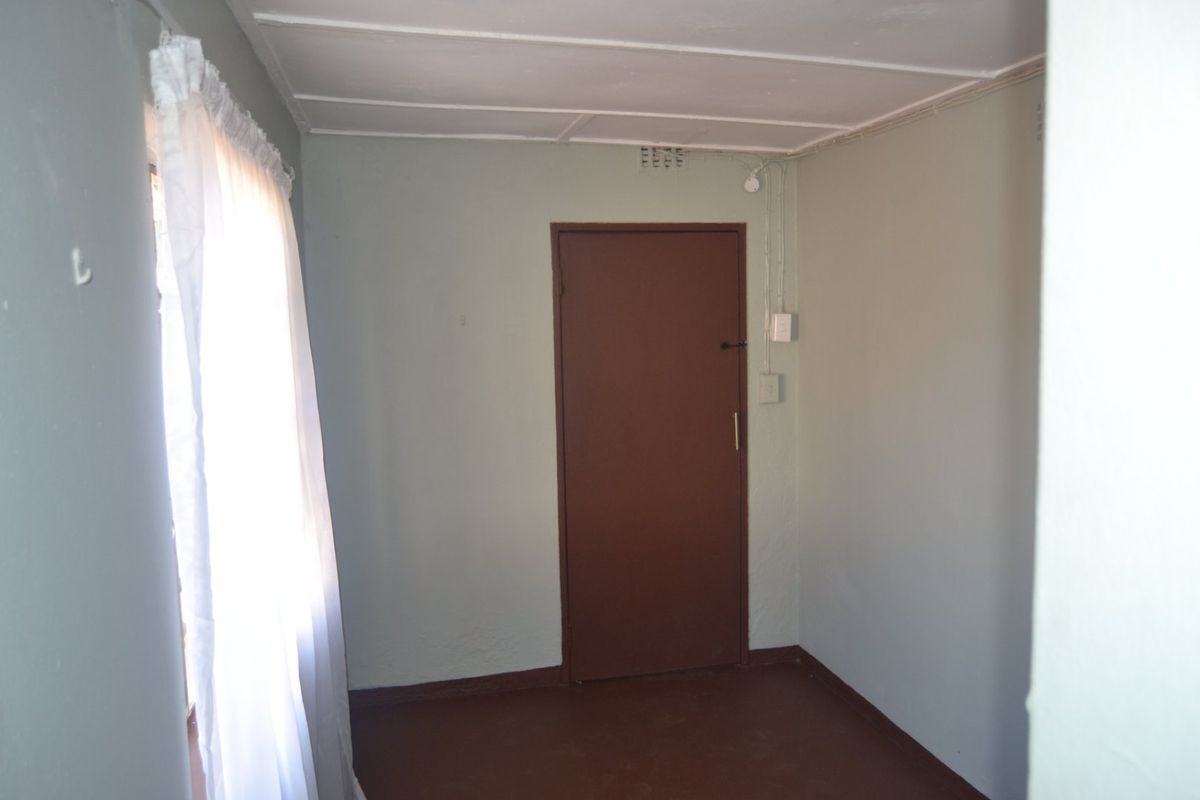 An empty bedroom featuring exposed electrical conduit, ceiling tiles, and a simple internal door, presenting a blank canvas for potential renovation.