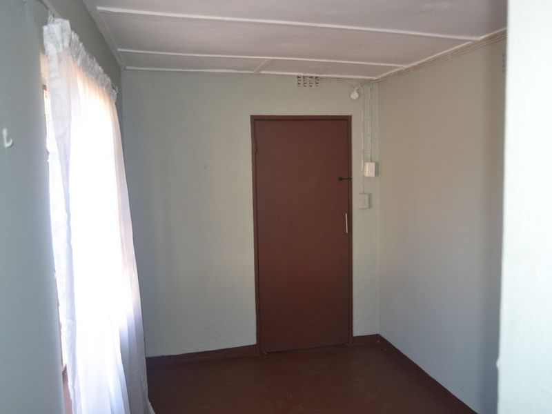 An empty bedroom featuring exposed electrical conduit, ceiling tiles, and a simple internal door, presenting a blank canvas for potential renovation.