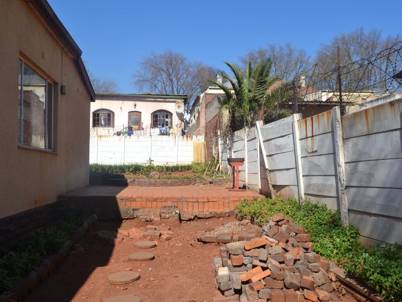 Rear exterior area featuring a brick paved patio, precast concrete boundary wall with razor wire, and an unlandscaped garden space requiring maintenance.