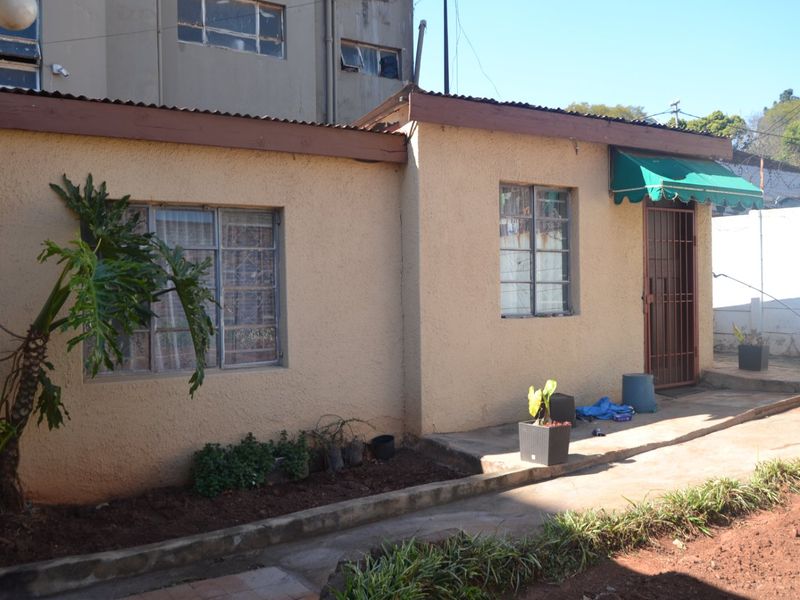 Rear exterior view of the property featuring textured plaster walls, steel-framed windows, a security gate, and a concrete pathway.