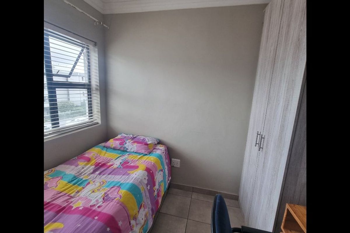 A compact bedroom featuring tiled flooring, a built-in wardrobe, and venetian blinds, providing a functional space with neutral wall finishes.