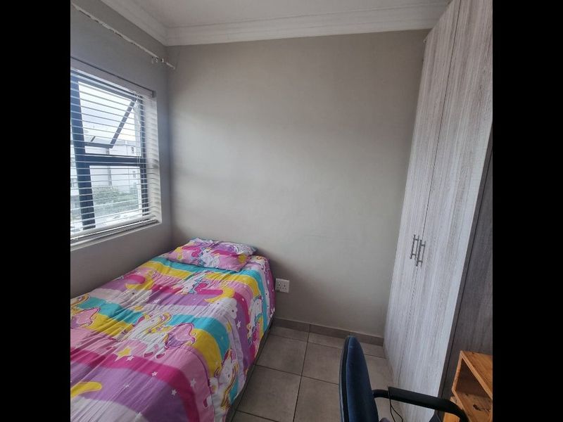 A compact bedroom featuring tiled flooring, a built-in wardrobe, and venetian blinds, providing a functional space with neutral wall finishes.