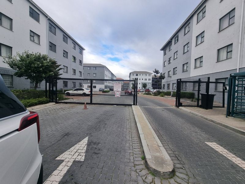 View of the apartment complex entrance featuring a secure gated access point, paved driveway, and perimeter fencing.