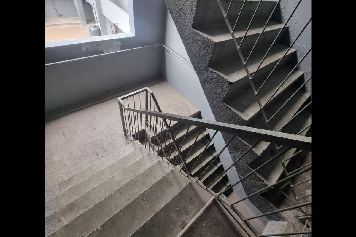 A functional concrete stairwell featuring metal balustrades, providing access between apartment levels with visible signs of wear and aging.