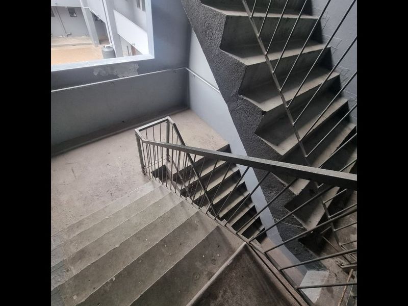 A functional concrete stairwell featuring metal balustrades, providing access between apartment levels with visible signs of wear and aging.