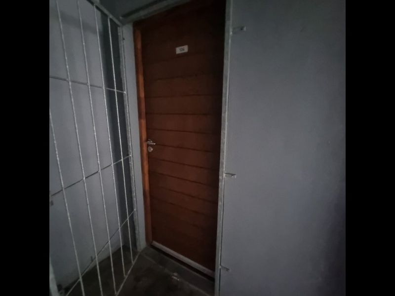 Entrance area featuring a solid timber door and a metal security gate in a basic apartment hallway setting.