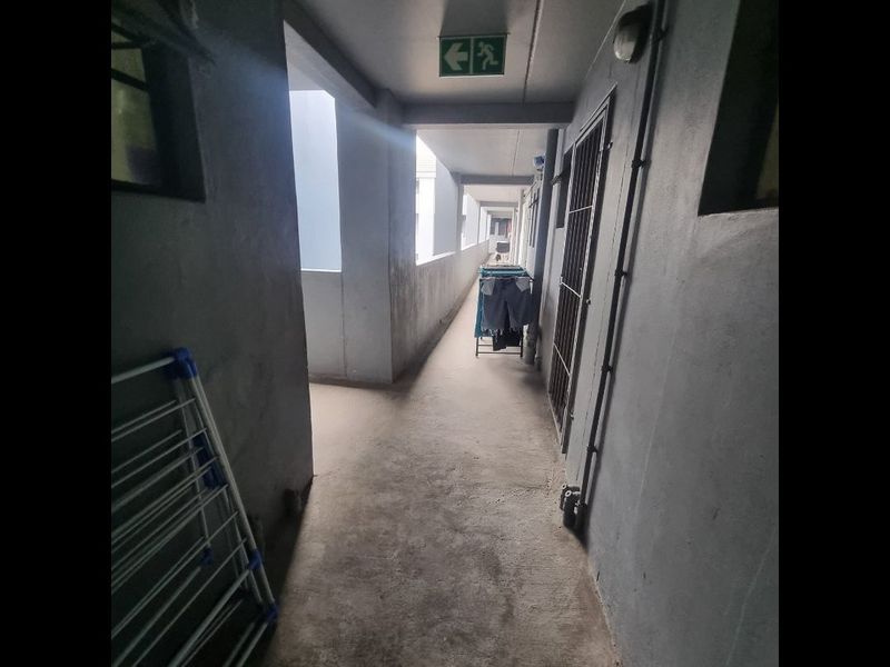 An exterior-facing apartment building hallway featuring concrete flooring, a security gate, and an emergency exit sign.