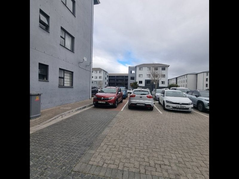 Exterior view of the apartment complex showing the paved parking area and building facade with security window bars.