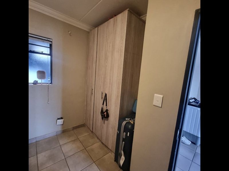 A bedroom featuring built-in cupboards, tiled flooring, and a window, providing a functional space with neutral wall finishes.