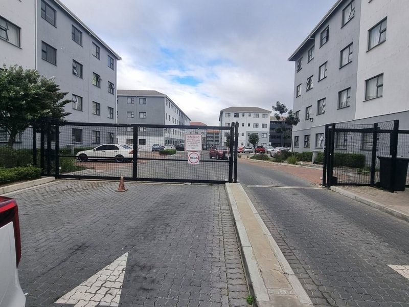 View of the apartment complex entrance featuring a secure gated access point, paved driveway, and multi-story residential buildings.