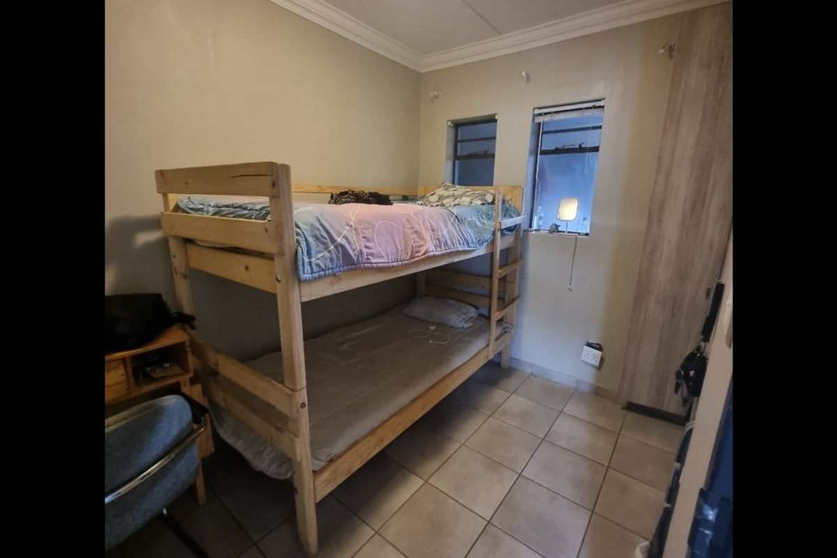 A functional bedroom featuring tiled flooring, a built-in wardrobe, and natural light from two casement windows.