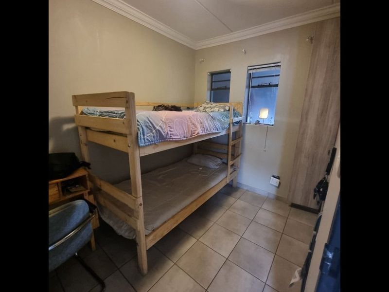 A functional bedroom featuring tiled flooring, a built-in wardrobe, and natural light from two casement windows.