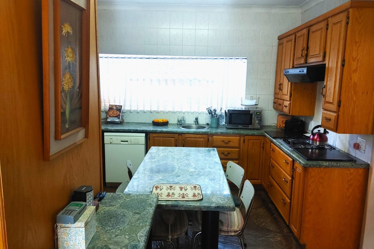 A functional kitchen featuring traditional wooden cabinetry, laminate countertops, a built-in hob with extractor fan, and a tiled backsplash.
