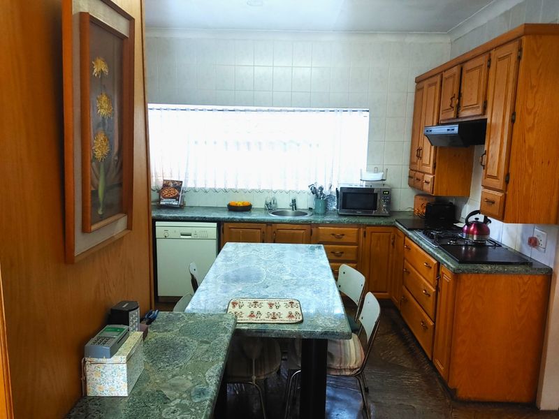 A functional kitchen featuring traditional wooden cabinetry, laminate countertops, a built-in hob with extractor fan, and a tiled backsplash.