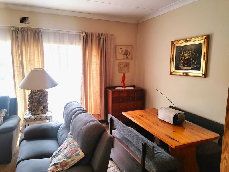 A living room featuring a sliding glass door with curtains, cove cornicing, and a wall-mounted air vent, showing signs of dated finishes.