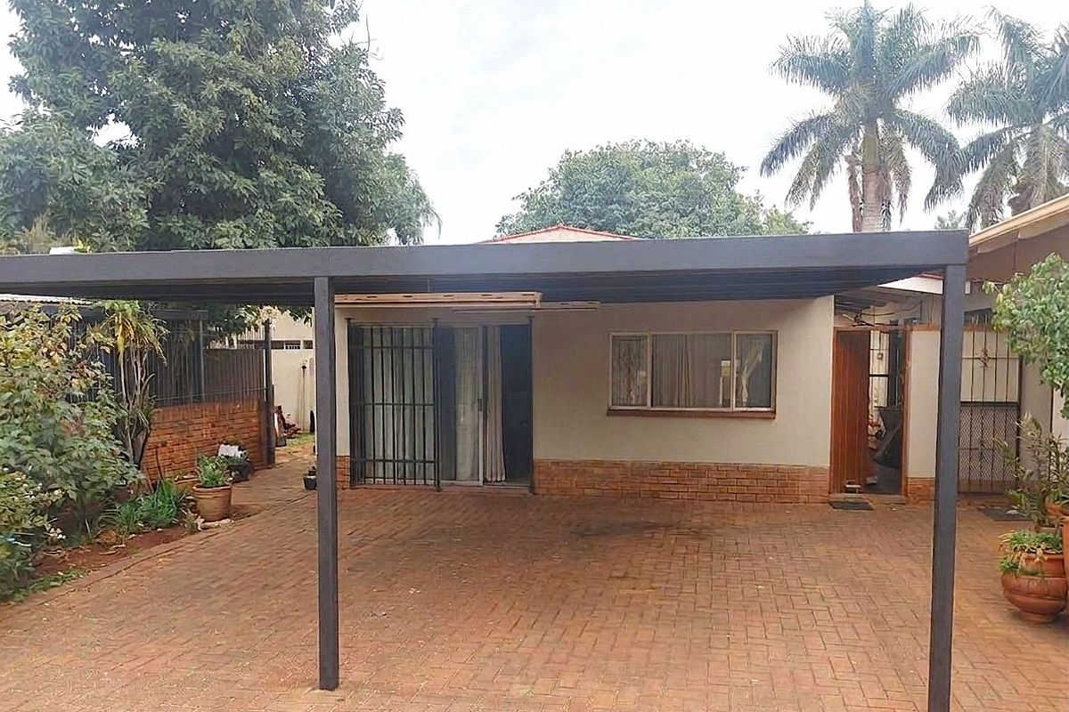 Rear exterior view featuring a covered carport, brick paved driveway, and secure access points to the main dwelling.