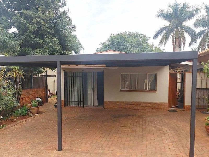 Rear exterior view featuring a covered carport, brick paved driveway, and secure access points to the main dwelling.