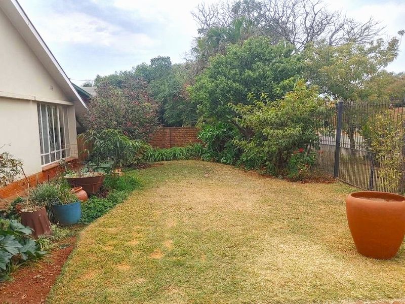 A private rear garden featuring a lawn, mature trees, and secure perimeter fencing with a brick boundary wall.