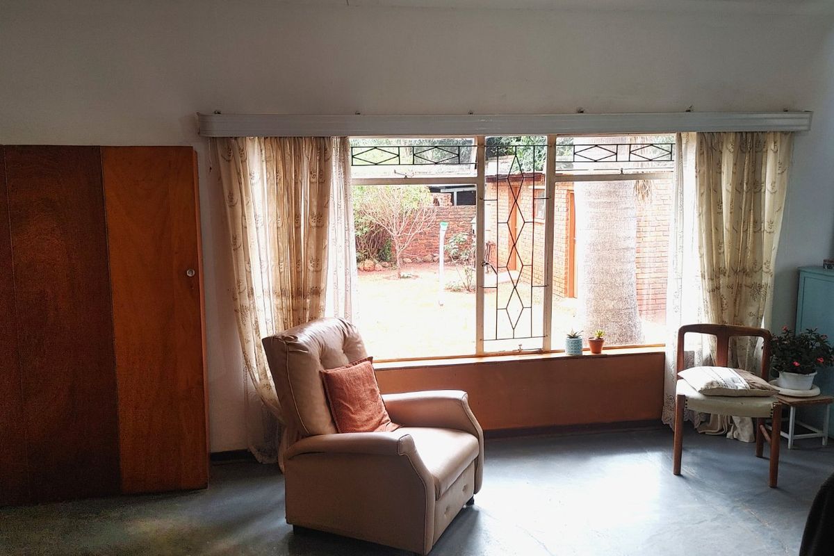 A bedroom featuring a built-in wooden wardrobe, large window with security bars, and painted concrete flooring, offering a view of the rear garden.