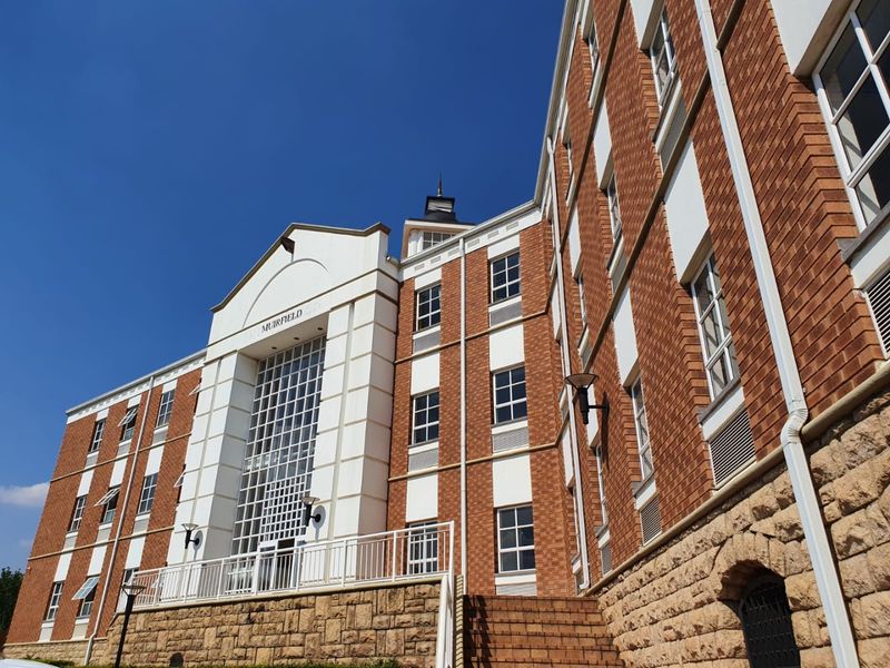 A low-angle view of the Muirfield commercial building facade, featuring a combination of red brick, stone cladding, and a prominent central glass entrance.