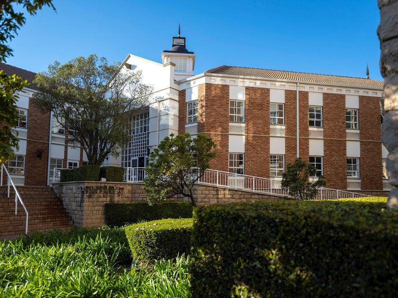 A well-maintained commercial building featuring a classic brick facade, a central cupola, and accessible ramp entry with landscaped garden surroundings.