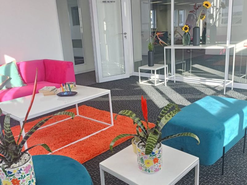 A modern commercial office breakout area featuring glass partitioning, carpeted flooring, and a bright, open-plan layout suitable for collaborative work.