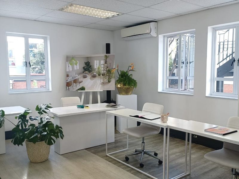 A bright, modern office space featuring laminate flooring, suspended ceilings with recessed lighting, and a wall-mounted air conditioning unit.