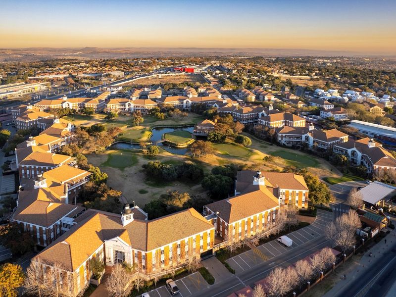 Aerial view of a large commercial office park featuring multiple buildings, central landscaped gardens with water features, and extensive paved parking facilities.