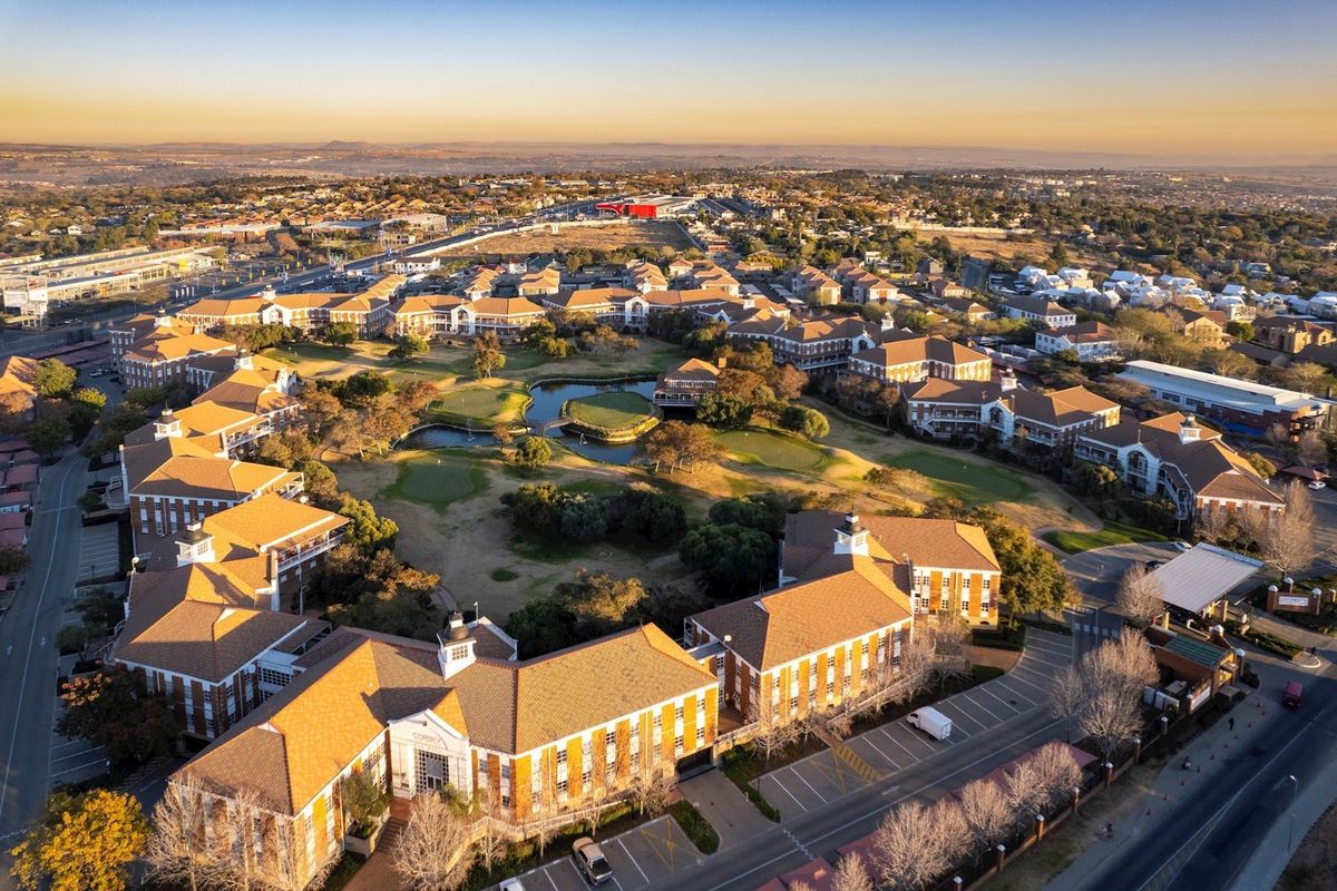 Aerial view of a large commercial office park featuring multiple buildings, central landscaped gardens with water features, and extensive paved parking facilities.
