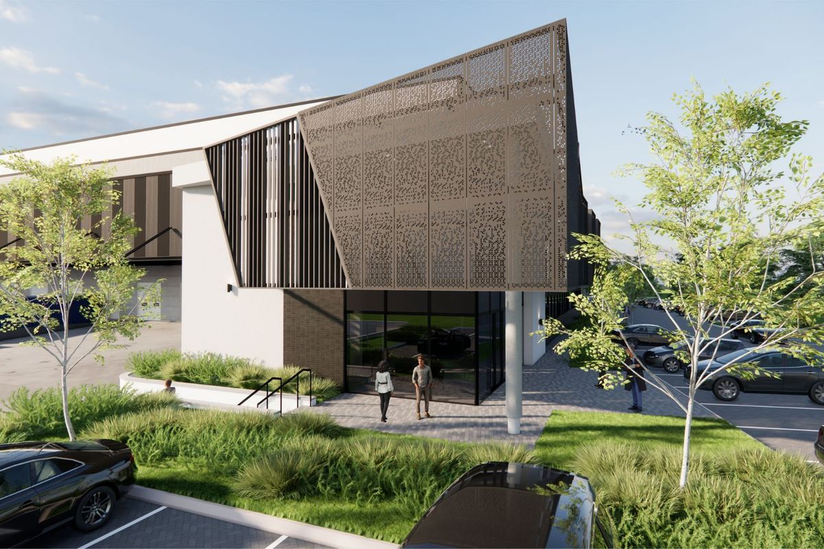 A modern industrial building exterior featuring a decorative metal screen facade, glass entrance, and landscaped parking area.