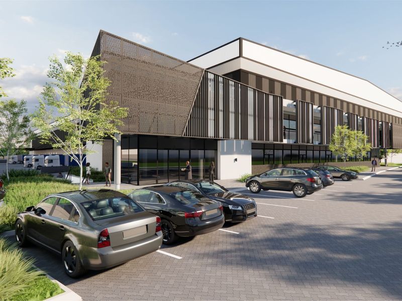 Modern industrial facility featuring a contemporary facade with perforated metal screens, extensive glass frontage, and a dedicated paved parking area.